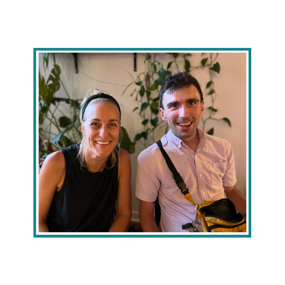 Kate is a white woman wearing a black shirt and Liam is a white male wearing a white short sleeved shirt and a cross-body bag. There are plants in the background.