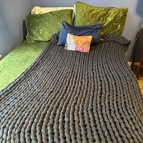 The Bearaby weighted blanket in dark gray-blue spread out over the end of a bed.